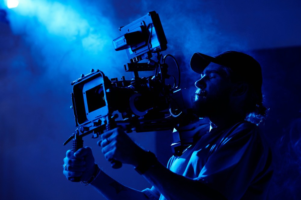 Cinematographer with a shoulder-mounted camera lit by blue haze